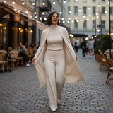 Woman in a beige outfit walking on a street with lights and people in the background