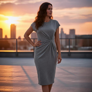 Woman in a gray dress standing on a rooftop with a city skyline and sunset in the background