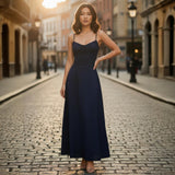 Woman in a long dark blue dress standing on a cobblestone street with buildings in the background.