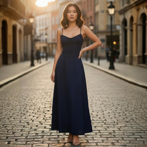 Woman in a long dark blue dress standing on a cobblestone street with buildings in the background.