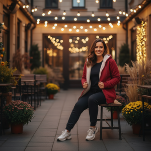 Woman sitting on a stool in an outdoor setting with string lights and plants.