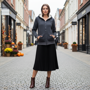 Woman wearing a dark gray hoodie and black skirt standing on a street with shops and decorative pumpkins.