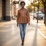 Woman walking on a sidewalk wearing a brown peplum top and ripped jeans.