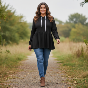 Woman wearing a black hoodie and blue jeans walking on a nature trail.