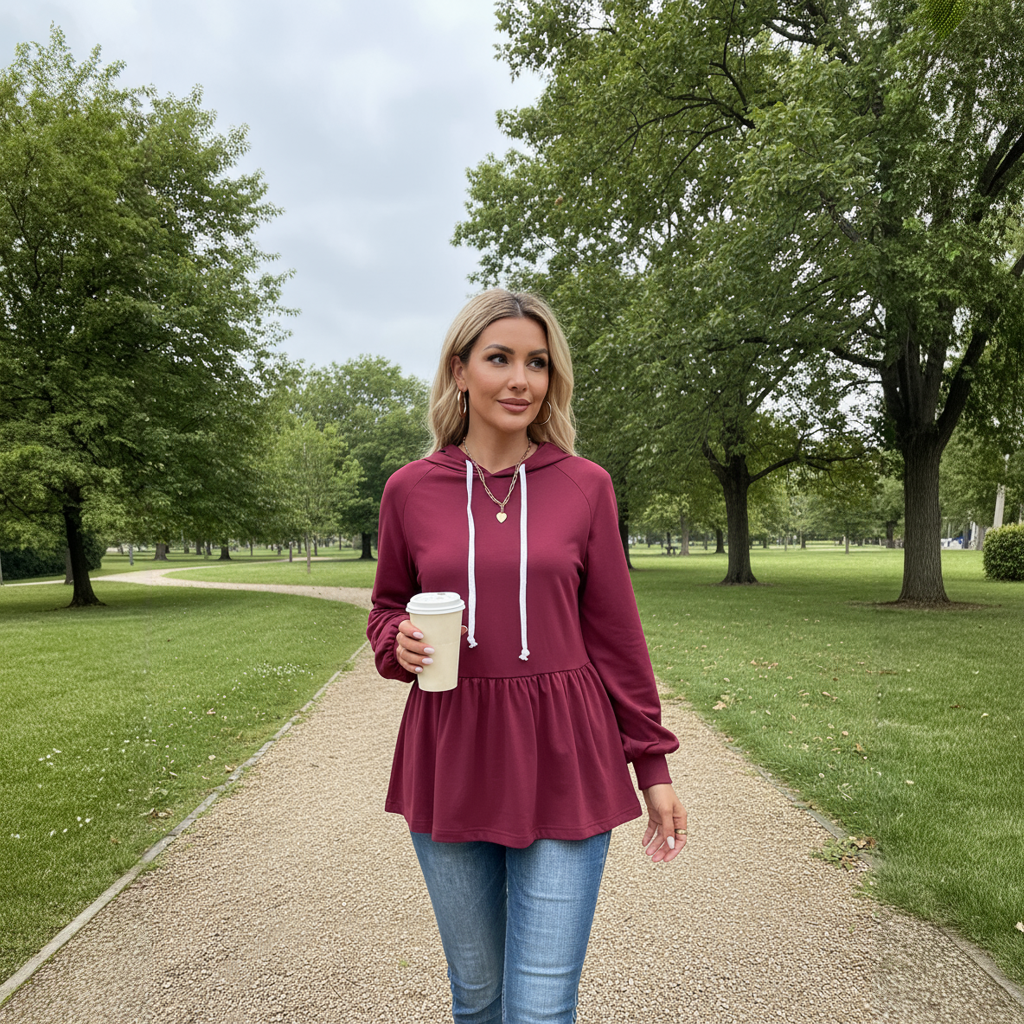 Woman wearing a burgundy hoodie and blue jeans walking in a park while holding a coffee cup.