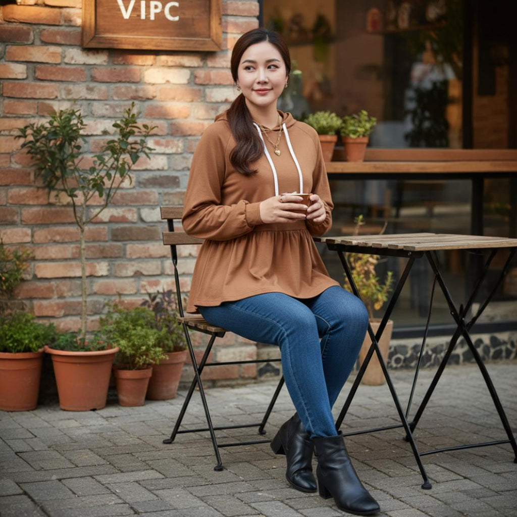 Woman sitting outdoors at a cafe, holding a cup, with a brick wall and potted plants in the background.