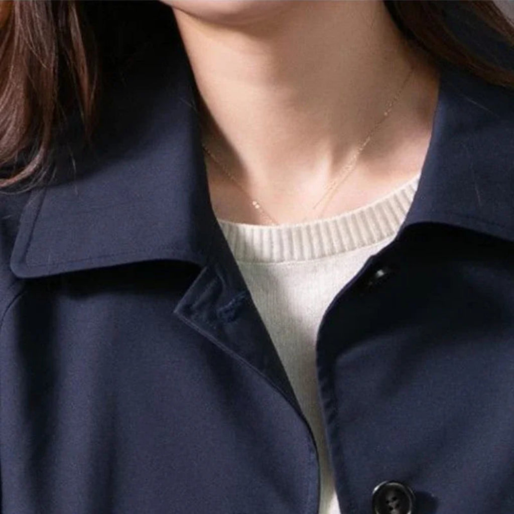 Person wearing a navy blue coat over a white sweater with a necklace.