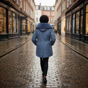 Person wearing a blue coat with fur hood walking down a wet street.