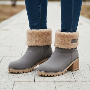 Gray ankle boots with beige fleece lining worn with blue jeans on a paved surface.