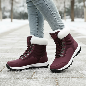 Maroon winter boots with white fur lining worn by a person on a snowy path.