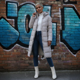 Person wearing a long puffer coat in front of a graffiti-covered brick wall