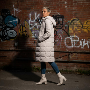Woman in a long puffer coat walking past a graffiti-covered brick wall.
