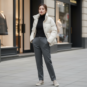 Woman wearing a white puffer jacket and gray pants standing on a city street.