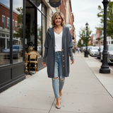 Woman walking on a sidewalk wearing a long gray coat, white shirt, and ripped jeans.