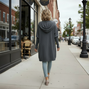 Woman walking on a sidewalk wearing a long gray coat, white shirt, and ripped jeans.