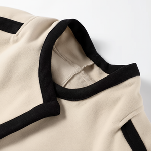Close-up of a beige garment with black trim on a white background